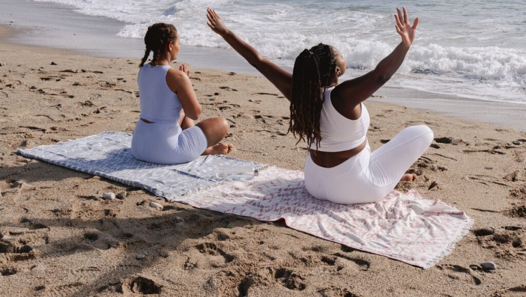 two people meditating on a beach 